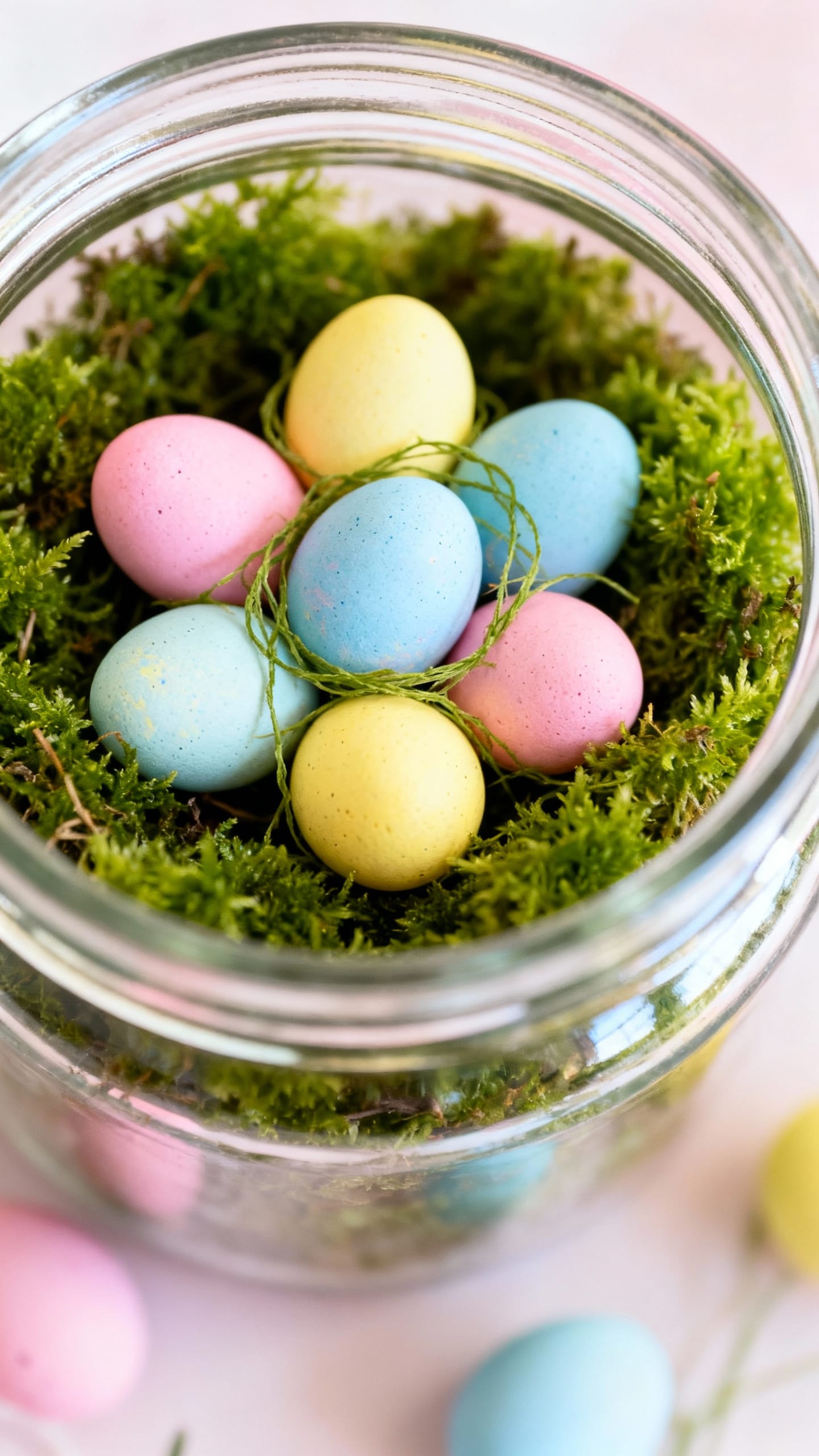 Closeup pastel-dyed eggs in moss-filled glass jar
